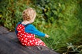 Cute adorable toddler girl sitting on wooden bridge and throwing small stones into a creek. Funny baby having fun with Royalty Free Stock Photo