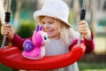 Cute adorable toddler girl swinging in domestic garden with soft plush toy. Happy healthy baby child in hat and dress Royalty Free Stock Photo