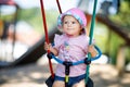 Cute adorable toddler girl swinging on outdoor playground. Happy smiling baby child sitting in chain swing. Active baby Royalty Free Stock Photo