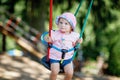 Cute adorable toddler girl swinging on outdoor playground. Happy smiling baby child sitting in chain swing. Active baby Royalty Free Stock Photo