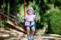 Cute adorable toddler girl swinging on outdoor playground. Happy smiling baby child sitting in chain swing. Active baby Royalty Free Stock Photo