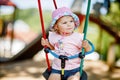 Cute adorable toddler girl swinging on outdoor playground. Happy smiling baby child sitting in chain swing. Active baby Royalty Free Stock Photo