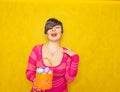 Pretty adult chubby woman with short hair holding colorful holiday eggs and a easter basket on yellow solid studio background