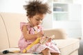 Cute African American child imagining herself as doctor while playing with stethoscope and toy on couch