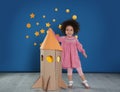 Cute African American child playing with cardboard rocket near wall
