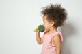 Cute African-American girl eating broccoli on white. Space for text