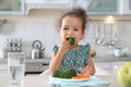 Cute African-American girl eating vegetables at table