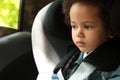 Cute African-American girl sitting in safety seat alone. Child in danger