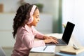 Cute african american girl teenager having online lesson, using laptop and headphones, sitting at desk, side view Royalty Free Stock Photo