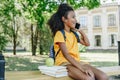 African american schoolgirl talking on smartphone while sitting on bench near books and apple Royalty Free Stock Photo