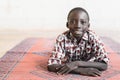 Cute African Boy with Toothy Smile Lying on an Africa Pattern Mat