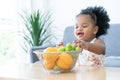 Cute African child girl smiling, choosing fruits from basket to eat at home. Happy little kid enjoy and having fun with tasty Royalty Free Stock Photo