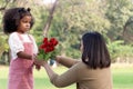 Cute African girl with black curly hair giving red rose flower to her mother while having a picnic at green garden park, Royalty Free Stock Photo