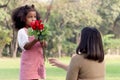 Cute African girl with black curly hair giving red rose flower to her mother while having a picnic at green garden park, Royalty Free Stock Photo