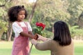 Cute African girl with black curly hair giving red rose flower to her mother while having a picnic at green garden park, Royalty Free Stock Photo