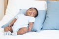 Cute African Nigerian newborn baby sleeping lying on pillow on white bed at home. Innocence infant with curly hair wear clothes Royalty Free Stock Photo