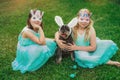 Cute Airedale Terrier dog in Easter bunny ears and little girls in bunny masks on Easter day sitting on grass in garden Royalty Free Stock Photo