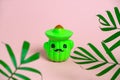 antistress cactus in hat toy and green tropical palm leaves on a pastel pink background Royalty Free Stock Photo