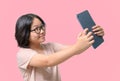 Cute asia girl wearing glasses takes a selfie of herself with a tablet on pink background Royalty Free Stock Photo