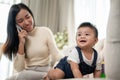 A cute Asian baby boy is crawling in the living room while his mom is talking on the phone Royalty Free Stock Photo