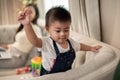 A cute Asian baby boy is playing with toys on a sofa while his mom is working on her laptop Royalty Free Stock Photo