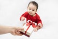 Cute asian baby in red bodysuit get gift box sitting on white blanket at home.Give Year present to child,kid,toddler.Concept Royalty Free Stock Photo