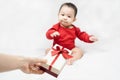 Cute asian baby in red bodysuit get gift box sitting on white blanket at home.Give Year present to child,kid,toddler.Concept Royalty Free Stock Photo