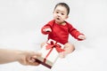 Cute asian baby in red bodysuit get gift box sitting on white blanket at home.Give Year present to child,kid,toddler.Concept Royalty Free Stock Photo