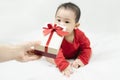 Cute asian baby in red bodysuit get gift box sitting on white blanket at home.Give Year present to child,kid,toddler.Concept Royalty Free Stock Photo
