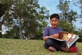 A cute boy reading a book in the park laughing