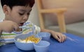 Cute Asian child eating breakfast and using spoon at home. Kid eating healthy food in kindergarten or at home Royalty Free Stock Photo