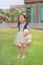 Cute Asian child girl dressed a fantasy outfit holding teddy bear and unshod walking on green grass garden with mother hand in