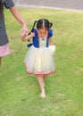 Cute Asian child girl dressed a fantasy outfit holding teddy bear and unshod walking on green grass garden with mother hand in