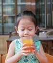 Cute asian child girl drinking Orange juice at restaurant Royalty Free Stock Photo