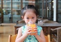 Cute asian child girl drinking Orange juice at restaurant with looking camera Royalty Free Stock Photo