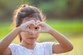 Cute asian child girl making heart shape with hands in the field