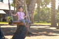 Cute Asian child girl sitting on wooden swing at resort in Thailand, swinging under palm tree, sand beach, hang medical mask on Royalty Free Stock Photo