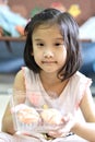 Cute Asian child girl is smiling while holding cupcakes.