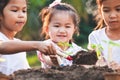 Cute asian children planting young tree in the black soil together in the garden