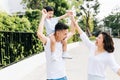 Cute Asian father piggybacking his son along with his wife in the park. Excited family raising hands together with happiness. Royalty Free Stock Photo