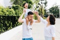 Cute Asian father piggybacking his son along with his wife in the park. Excited family raising hands together with happiness. Royalty Free Stock Photo