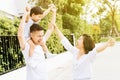 Cute Asian father piggybacking his son along with his wife in the park. Excited family raising hands together with happiness. Royalty Free Stock Photo