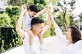 Cute Asian father piggybacking his son along with his wife in the park. Excited family raising hands together with happiness. Royalty Free Stock Photo