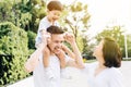 Cute Asian father piggybacking his son along with his wife in the park. Excited family spending time together with happiness.