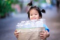 Cute Asian girl carries paper bag full of plastic water bottles. Children sort out trash for recycling.