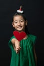 Cute asian girl child dressed in a green dress holding a Christmas ornament and a heart stick on a black background Royalty Free Stock Photo