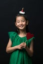 Cute asian girl child dressed in a green dress holding a Christmas ornament and a heart stick on a black background Royalty Free Stock Photo