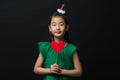 Cute asian girl child dressed in a green dress holding a Christmas ornament and a heart stick on a black background