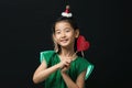 cute asian girl child dressed in a green dress holding a Christmas ornament and a heart stick on a black background Royalty Free Stock Photo