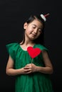 Cute asian girl child dressed in a green dress holding a Christmas ornament and a heart stick on a black background Royalty Free Stock Photo